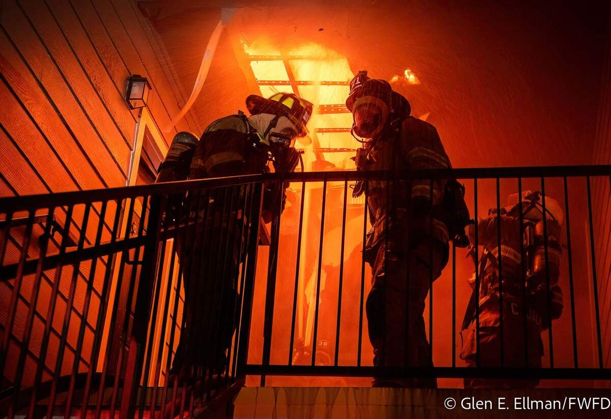 Two firefighters stand in front of a wall of flames.