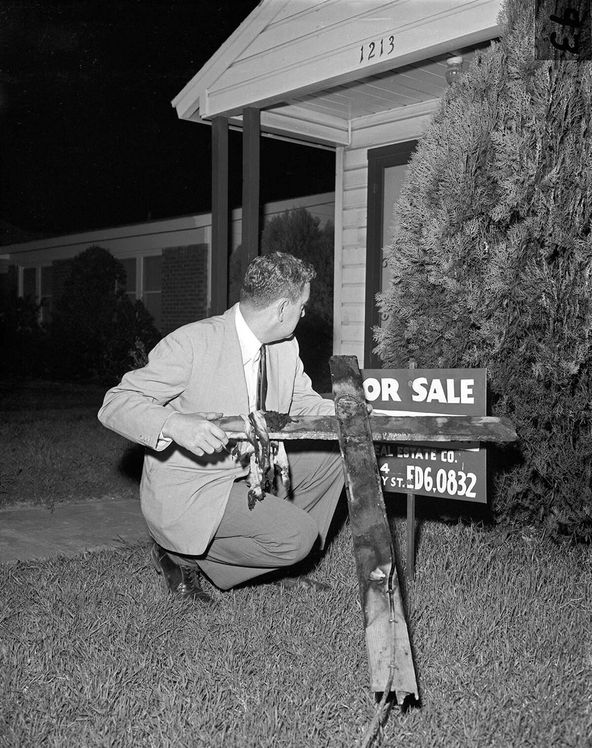 A reporter holds a cross burned in the yard of a Morningside home purchased by a Black family in April 1960. By this time, many homes in the neighborhood owned by White people were for sale.