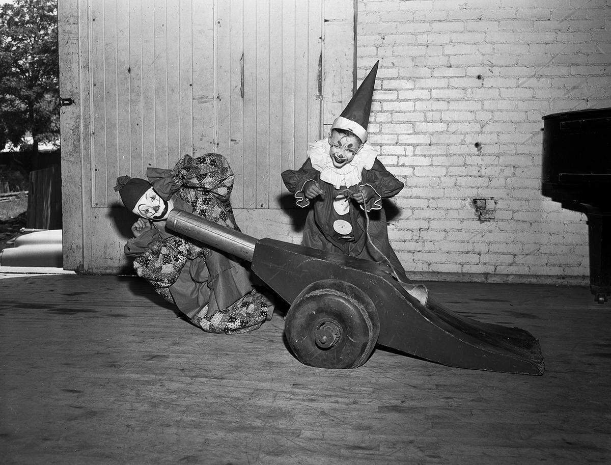 Two clowns pose with a fake cannon, with one smiling and looking into the barrel.