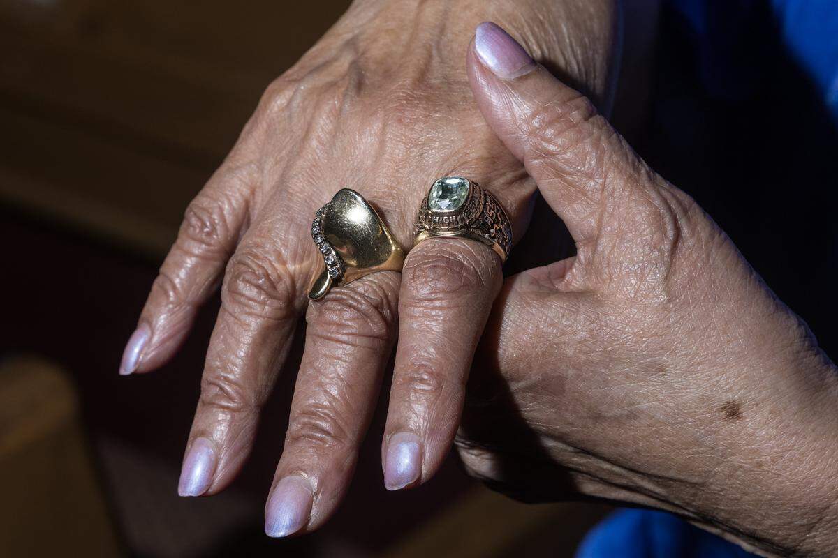 A detail photograph of an older woman’s hands; a large ring is on the middle finger and a ring with a gemstone is on the ring finger.