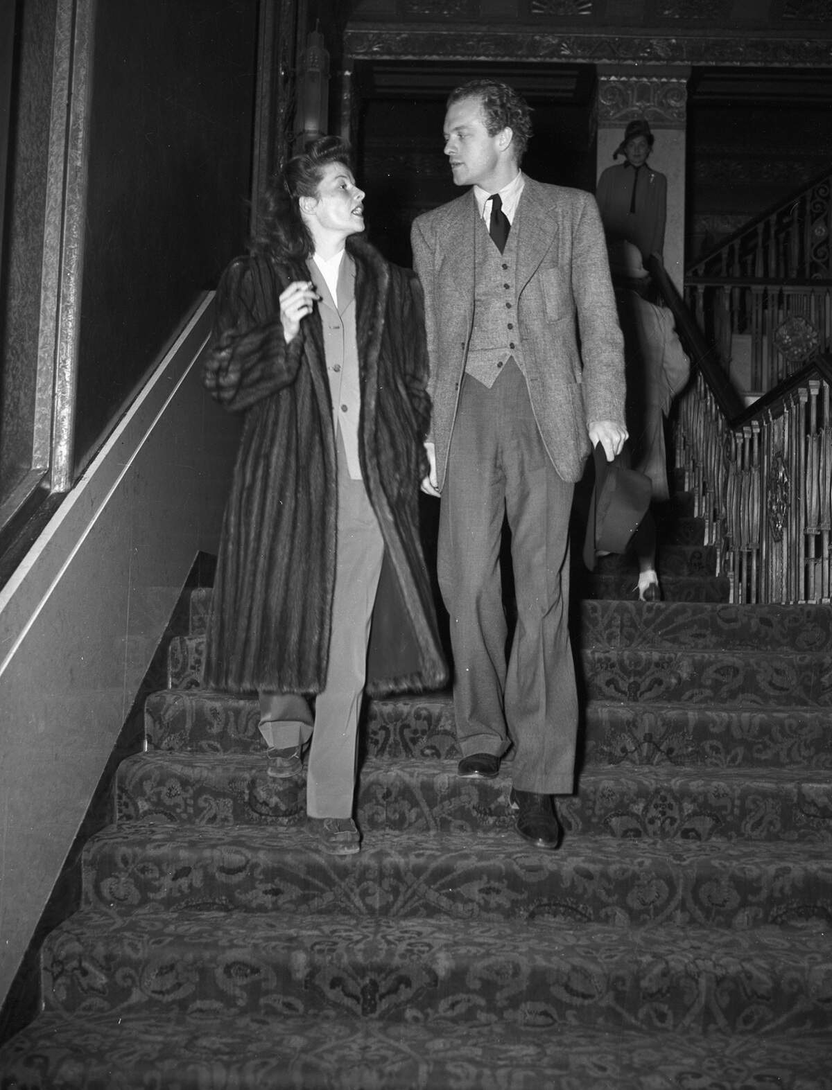 Hepburn is wearing a mink coat, slacks and oxfords. She is holding a cigarette in her right hand. Mr. Heflin is wearing a three-piece suit and is holding his hat in his left hand.