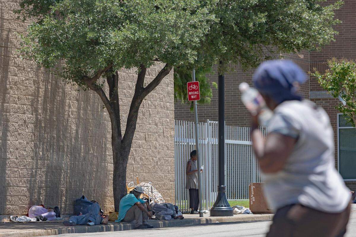 A woman presses a water bottle to her face while crossing the street outside of the Union Gospel Mission in Fort Worth, Texas, on Friday, July 8, 2022.