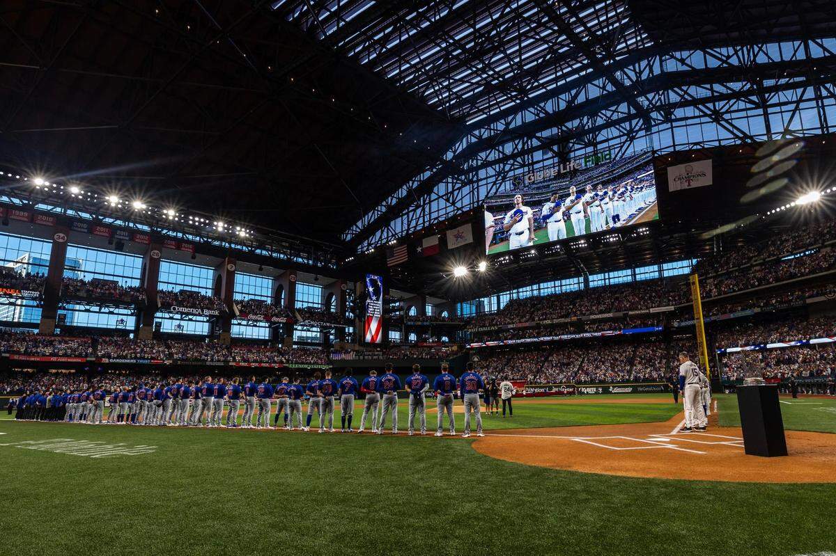 The Chicago Cubs and Texas Rangers line up while the National Anthem is performed prior to the season opener at Globe Life Field in Arlington on Thursday, March 28, 2024.