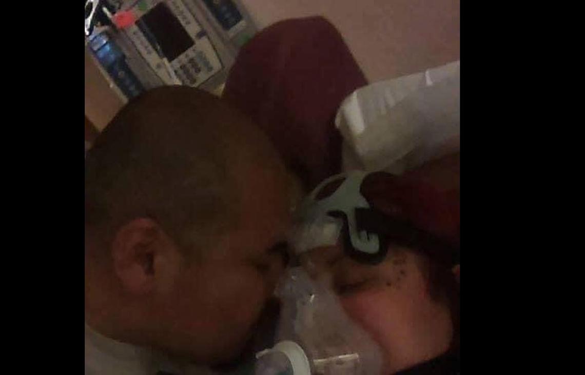 Manuel Castro (left) leans in to give his wife, Sandra Castro (right), a kiss on the cheek as she lies in a hospital bed with the coronavirus. He and their children have often not been allowed to see her during her hospital visits, which has been a challenge for all of them.