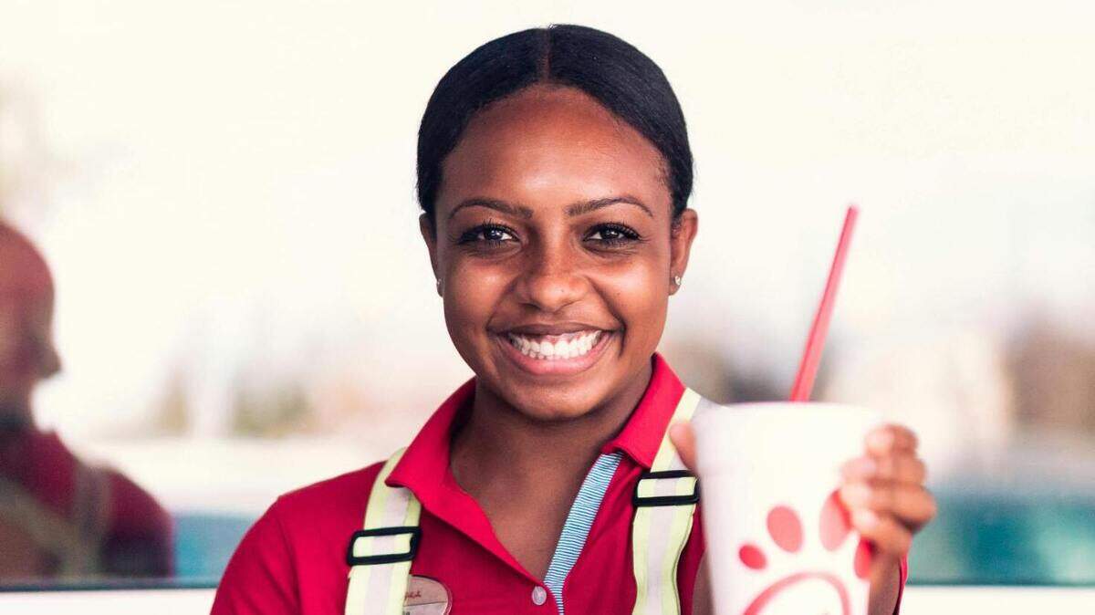 Chick-Fil-A employee sitting at a table holding a drink cup.