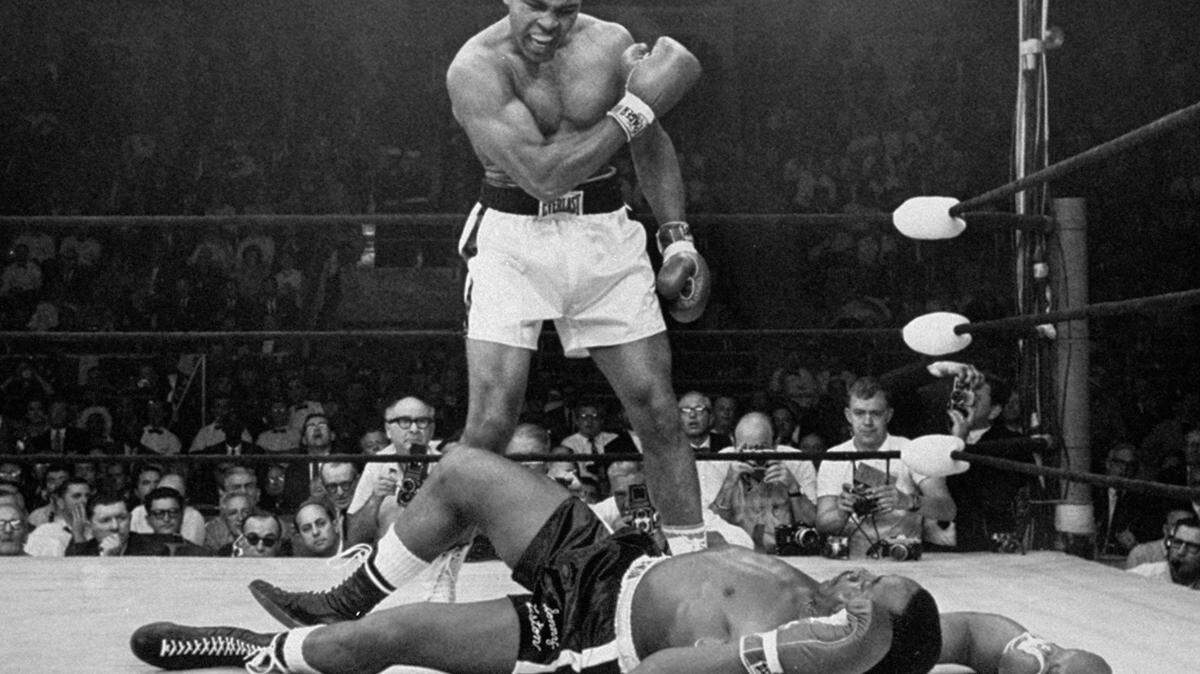 FILE - In this May 25, 1965, file photo, heavyweight champion Muhammad Ali stands over fallen challenger Sonny Liston shortly after dropping him with a short hard right to the jaw in Lewiston, Maine.  The Louisville Regional Airport Authority’s board voted in 2019, to change the name to Louisville Muhammad Ali International Airport. Ali would have turned 77 Thursday. He died in 2016. (AP Photo/John Rooney, File)