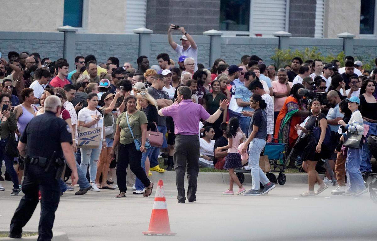 People gather across the street from the Allen Premium Outlets following a shooting on Saturday.
