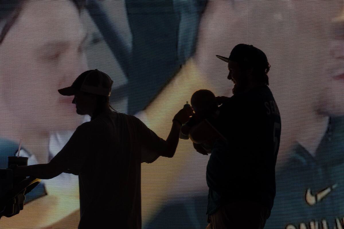 Isabel and Hank Thompson carry their son Liam, 3 months, past an LED screen showing MLB highlights on the first day of the 2024 MLB All-Star Village at Choctaw Stadium in Arlington on Saturday, July 13, 2024.