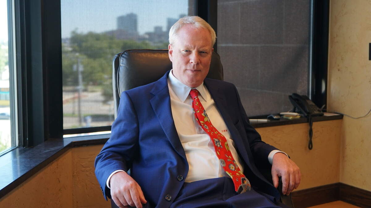 A blond haired man in a blue suit sitting in an office. 