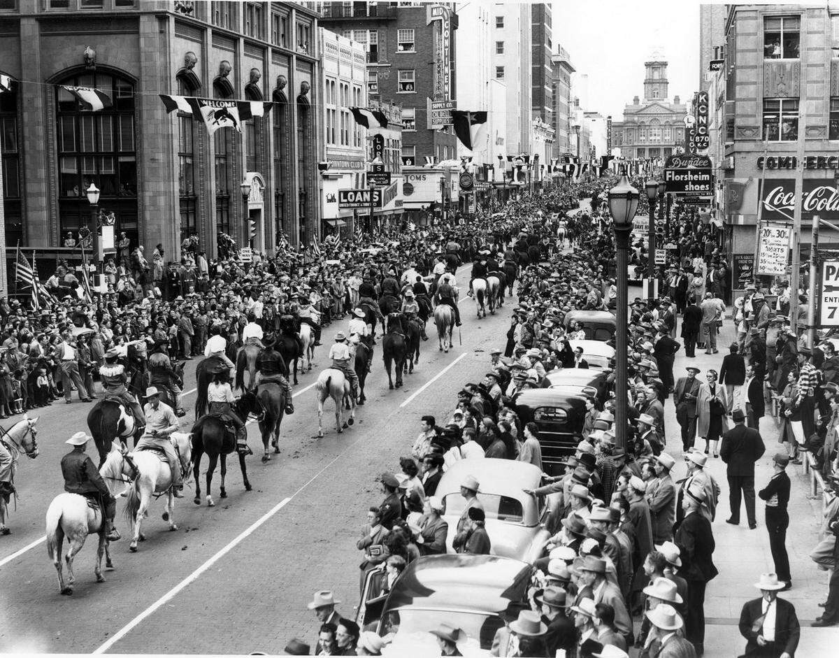 1953: &nbsp;The Stock Show parade nears the intersection of 7th and Main streets, heading north towards the Tarrant County Courthouse. American flags and Stock Show banners line the street. Businesses fronting the parade route include the Jack Collier Drug Co., KONC Radio, Dundee men’s clothier, Mid-Continent Supply, United Finance and Thrift Co., and the Downtown Club, a billiard hall.