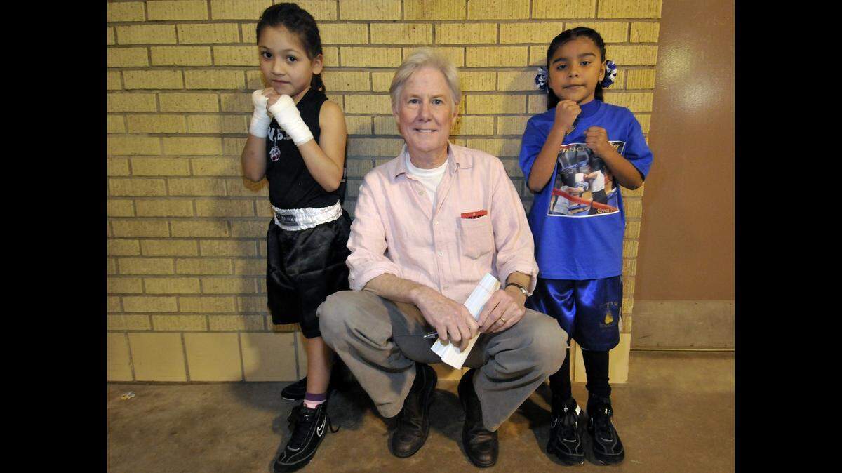 A man crouched down between two 8-year-old boxers. 