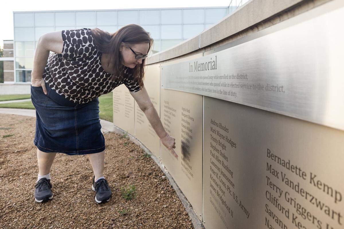 Amy Kirkland bends down to point to a name on a brown curved wall outside a building.