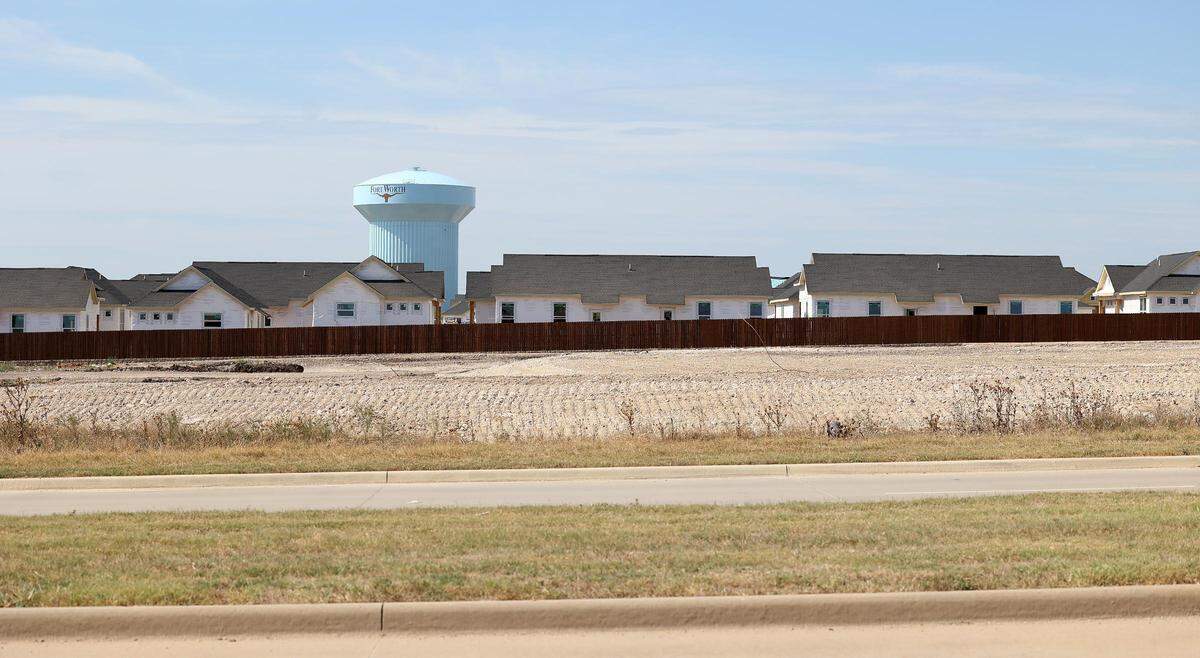 A housing development under construction with a suburban road in the foreground and a water tower in the distance.
