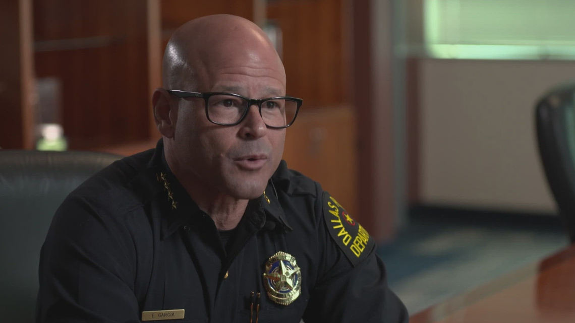 A bald guy with glasses in a police uniform sitting down in a TV interview. 