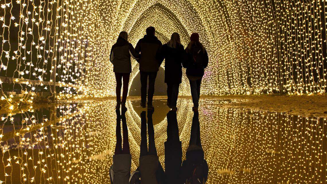 The black silhouettes of a group of four people contrast a golden arch illuminated with thousands of lights.