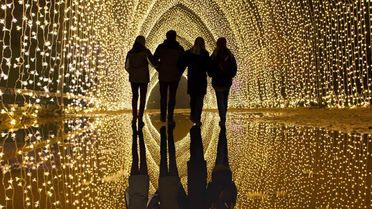 The black silhouettes of a group of four people contrast a golden arch illuminated with thousands of lights.