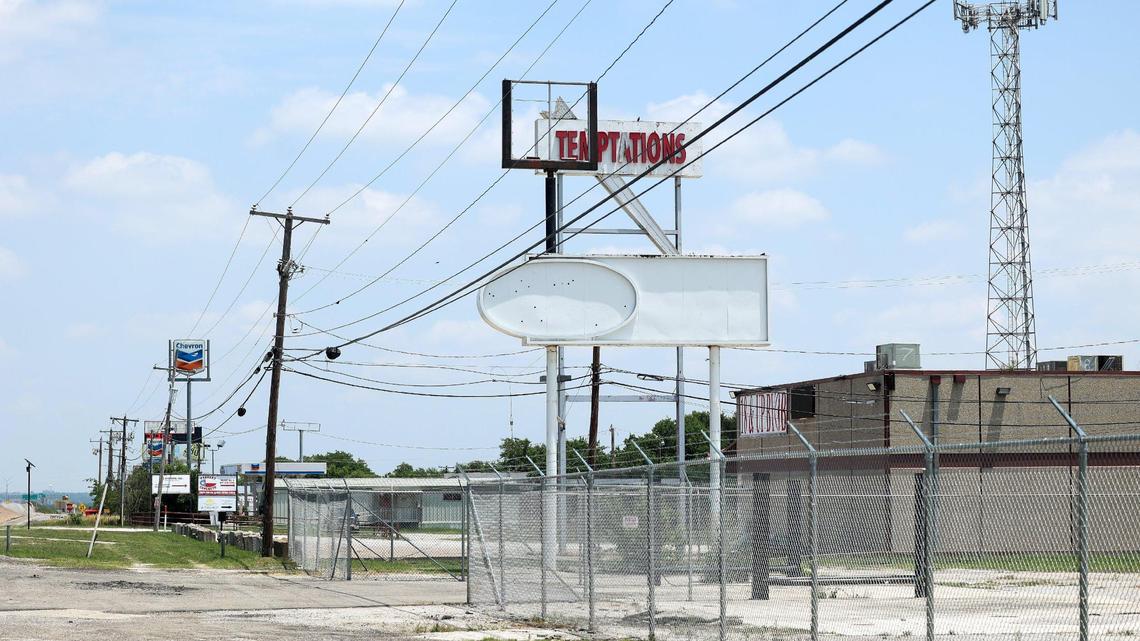 A view down the side of a road with lots of power lines and fencing. A sign reading 'Temptations' can be seen half way down,.