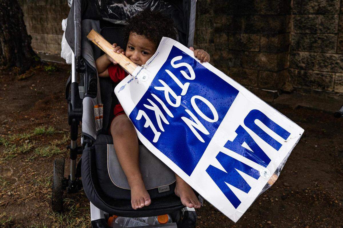 19-month-old son Auhsten Bartlett holds a sign in support of his father and General Motors employee Edward Bartlett while on strike outside of the General Motors Assembly Plant in Arlington on Tuesday, Oct. 24, 2023. Bartlett is a temporary employee at the assembly plant and said he isn’t making enough to support his family. “When I am making $16 an hour and the person next to me is making $30 an hour doing the same job, it’s just unfair.”
