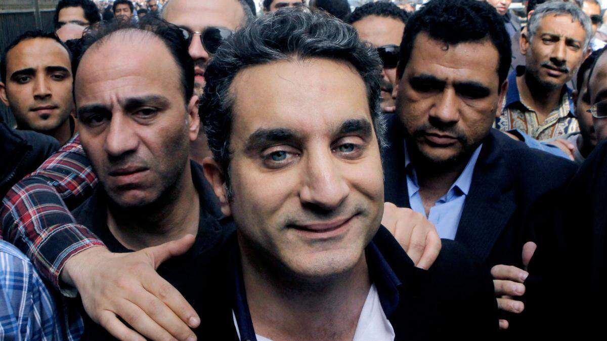 FILE - In this Sunday, March 31, 2013 file photo, a bodyguard secures popular Egyptian television satirist Bassem Youssef, who has come to be known as Egypt’s Jon Stewart, as he enters Egypt’s state prosecutors office to face accusations of insulting Islam and the country’s Islamist leader in Cairo, Egypt. After more than four months away, the man known as Egypts Jon Stewart returns the airwaves Friday in a country radically different from the one he previously mocked. Satirist Bassem Youssefs weekly El-Bernameg, or The Program in Arabic, mocked the countrys first elected Islamist president and his supporters for mixing religion and politics, took them to task for failing to be inclusive or deliver on peoples demands for change_ to the extent that some said he was one of the main reasons people turned against Mohammed Morsi. (AP Photo/Amr Nabil, File)