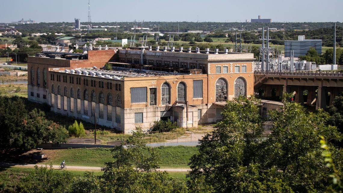 An old two story brick power plant sitting on a mostly empty island. 