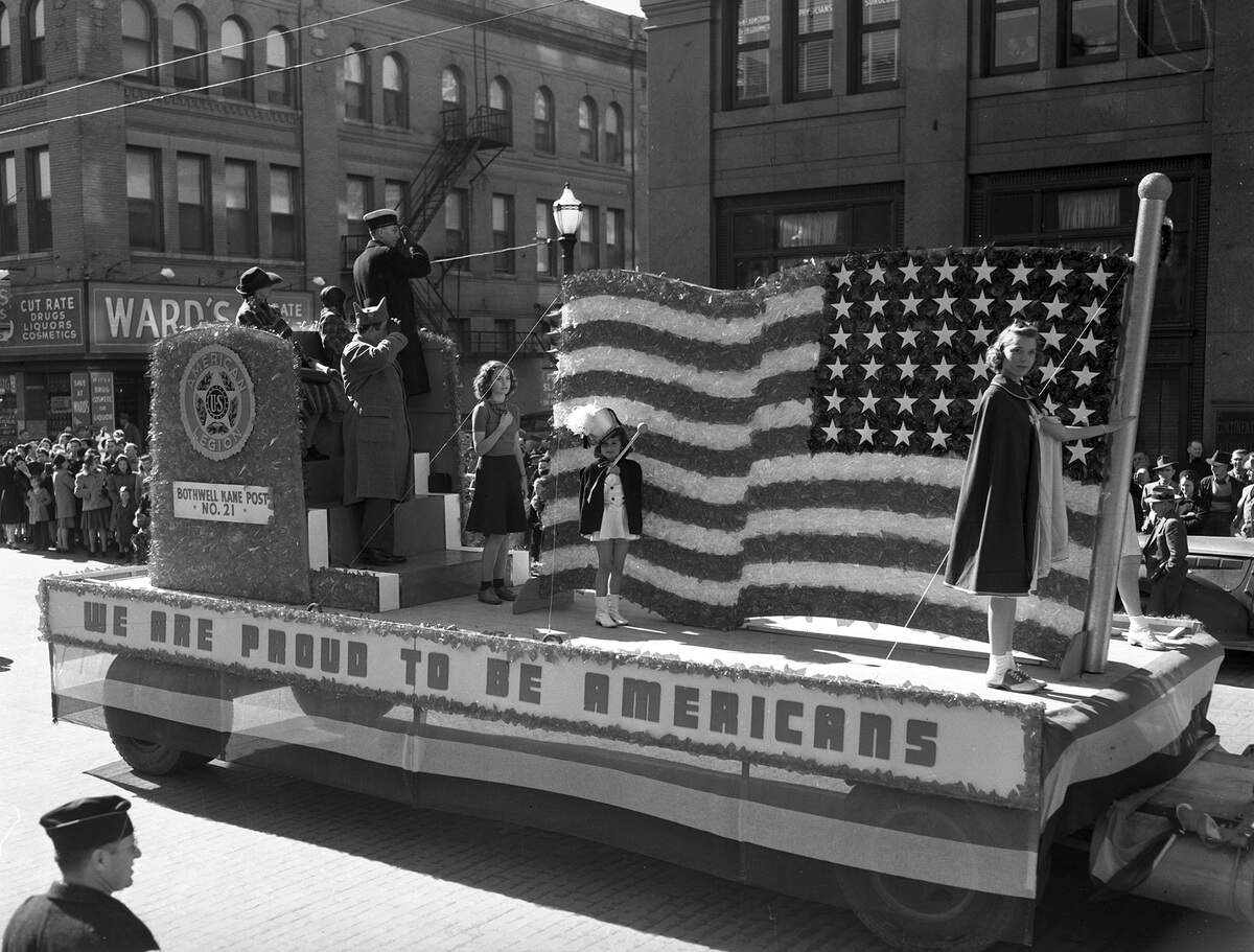 Nov. 11, 1940: Armistice Day parade showing the float entered by the Bothwell Kane Post no. 21, American Legion bears a huge American flag made of red, white and blue cellophane and a banner that reads “We are proud to be Americans.” The parade stopped for a minute at 11 a.m. for the men to face west and salute in honor of the World War dead.