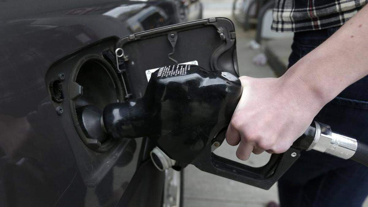 A hand places a fuel nozzle into the opening of a gas tank.