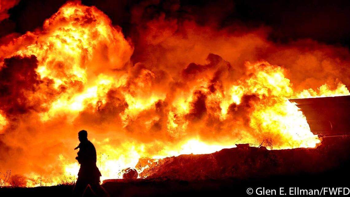 A Fort Worth firefighter walks in front of a large mulch fire that began after midnight Sunday at Living Earth on Salt Road. The fire was still burning as of 3 p.m. Sunday.