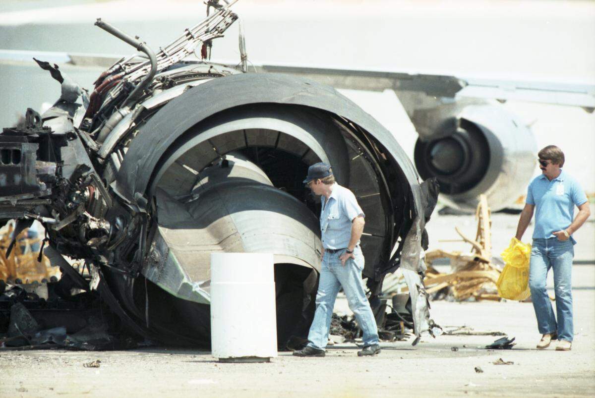 Two men walk around the destroyed turbine of a plane that is much taller than them.