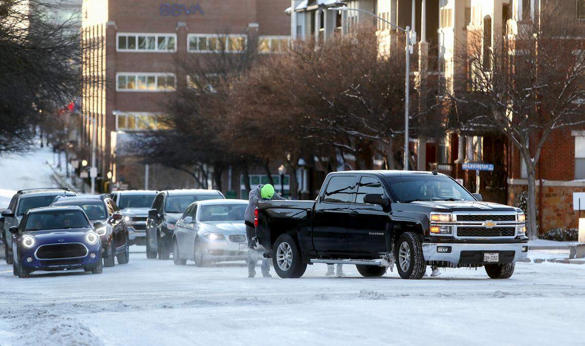 A man helps to push a truck off a patch of ice at the intersection of West 7th Street and Henderson Street on Feb. 15, 2021, in Fort Worth.