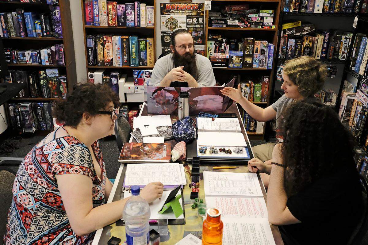 In this July 17, 2019, photo Zayah Abel rolls the dice during a game of Dungeons and Dragons with Norah Wright, bottom right, Sarah Melton, left, and Keith Surman, center, at Castle Perilous in Carbondale in Carbondale, Ill. (Isaac Smith/The Southern Illinoisan via AP)