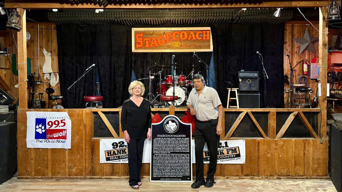 Owners Jean and Kiran Desai proudly pose in front of the historical marker and the iconic Stagecoach Ballroom stage.
