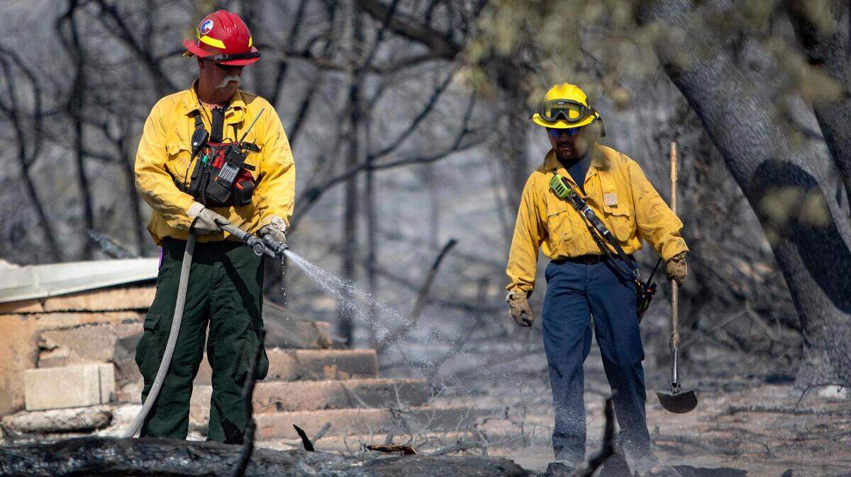 Firefighters spray water on the remains of a smoldering structure on Possum Kingdom Lake in Graford, Texas, on Wednesday, July 20, 2022.