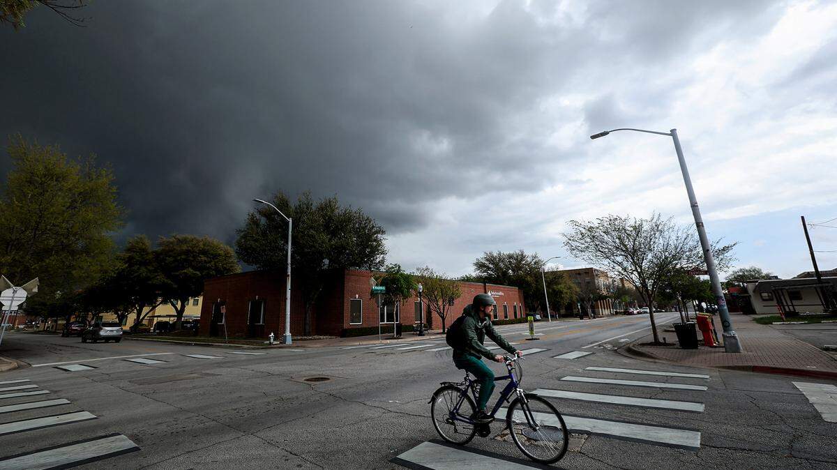 Storm clouds move over a corner of West Magnolia Street in Fort Worth. A person on a bike is at the forefront heading to the right of frame.