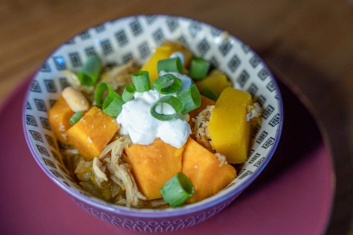 A bowl of pumpkin chicken chili in a bowl, garnished with sour cream and green onions.