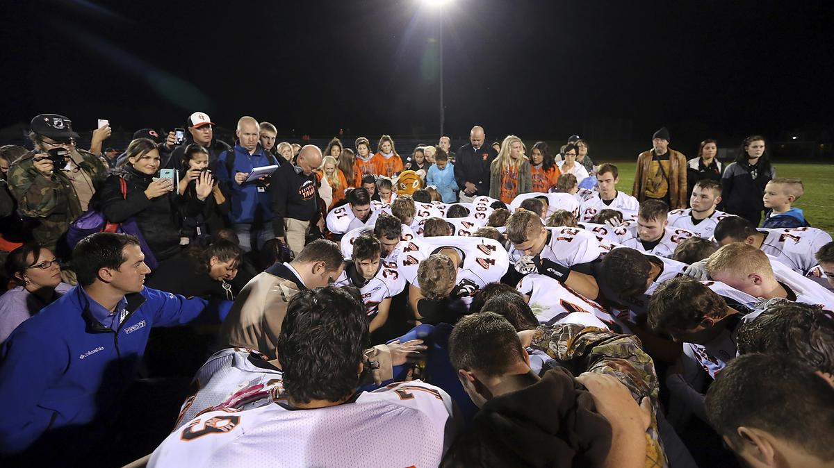 FILE - Bremerton assistant football coach Joe Kennedy, obscured at center in blue, is surrounded by Centralia High School football players as they kneel and pray with him on the field after their game against Bremerton on Oct. 16, 2015, in Bremerton, Wash. After losing his coaching job for refusing to stop kneeling in prayer with players and spectators on the field immediately after football games, Kennedy will won his case before the U.S. Supreme Court. (Meegan M. Reid/Kitsap Sun via AP, File)