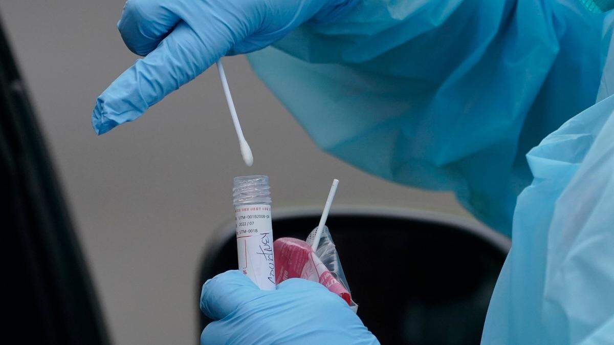 Gloved hands insert a COVID test swab into a plastic tube at a drive-thru testing location.