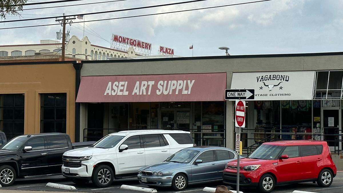 The front of Asel Art Supply's West 7th location shows a red awning and white letters. It sits next to Vagabond Vintage Clothing.