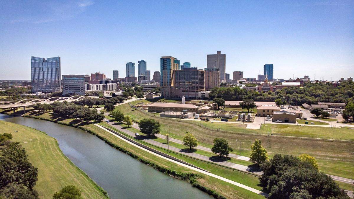 A view of Fort Worth's downtown skyline, taken from a drone, showing the Trinity River in the foreground and highrise buildings in the background.