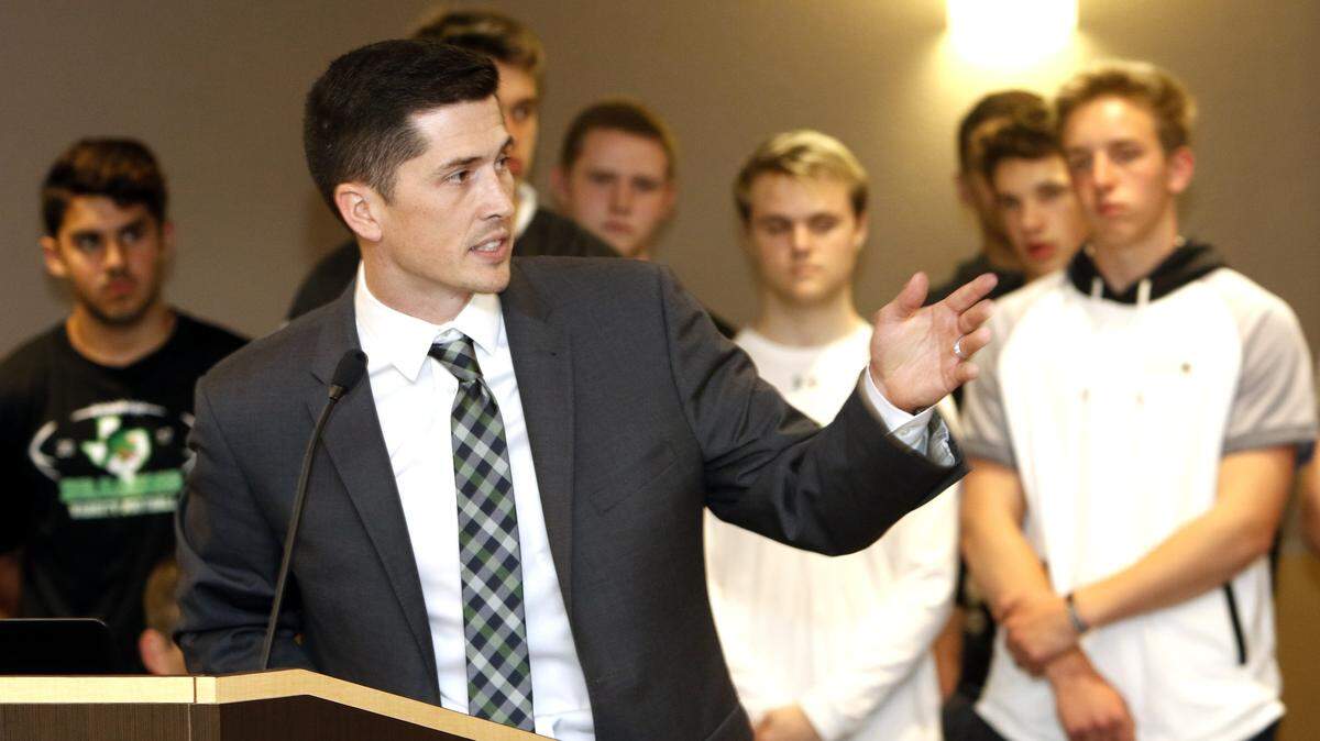 With Dragon football players in the background, Riley Dodge is introduced as the new head coach during a Carroll school board meeting March 26, 2018.
