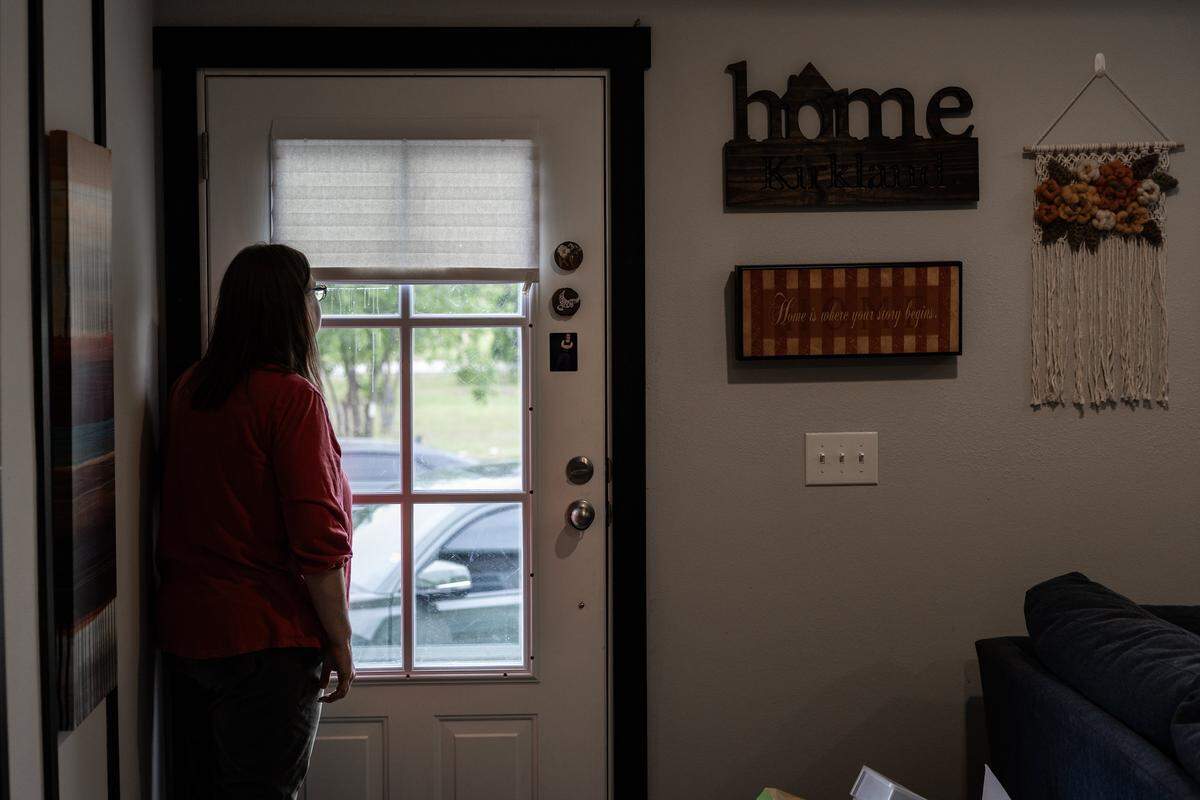 Amy looks out the glass window of her front door. To the right is a sign that says ‘home.’