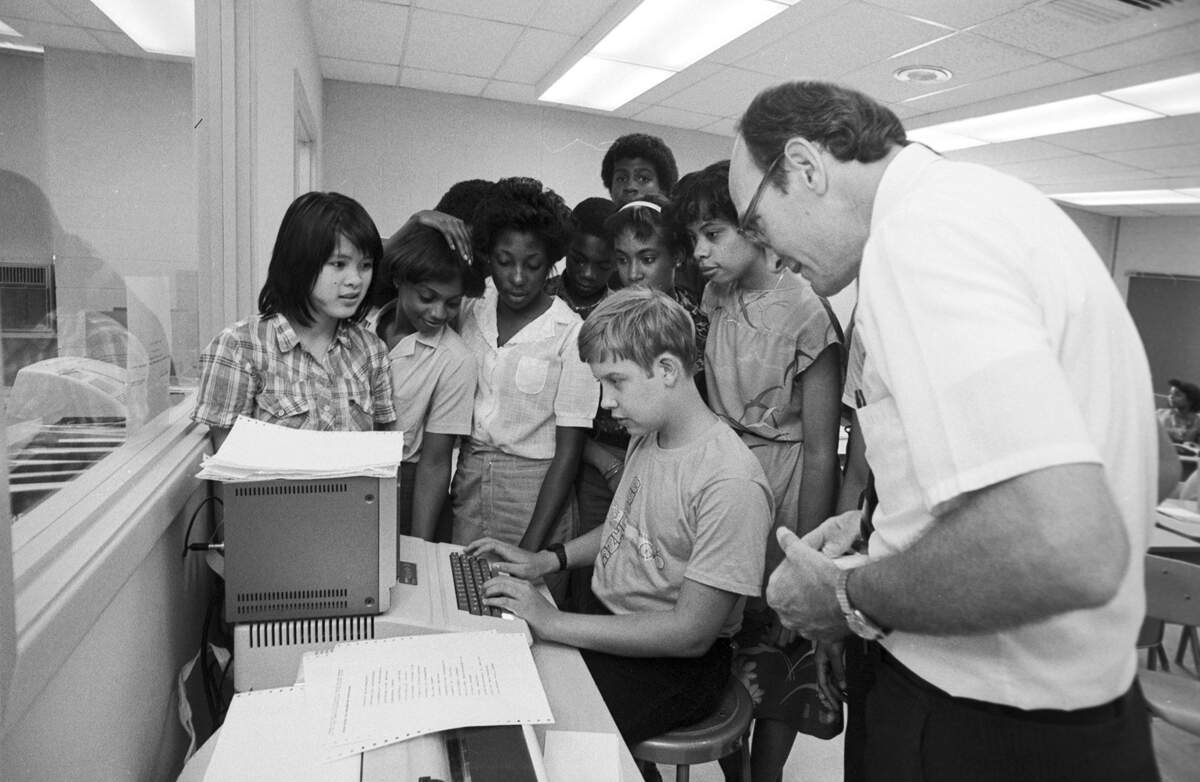 Teacher Gary Hicks, right, along with Yen Nguyen, left, crowd around Jerry Grimm, seated at a terminal during the first day at school at Dunbar High, the last school in the Fort Worth district to implement integration of non-African-American students. The students are part of a magnet program