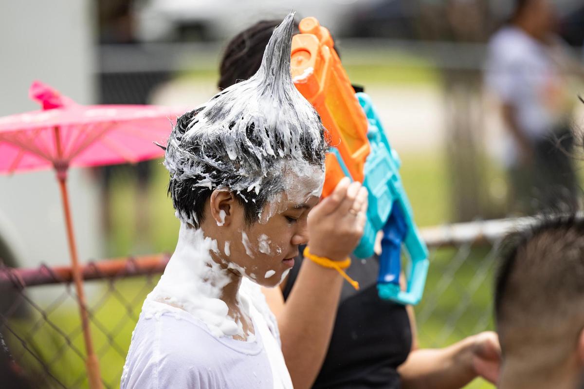 A festival attendee styles his hair with shaving cream for the Lao New Year parade on the third day of the Lao New Year festival at Wat Lao Thepnimith Temple in Saginaw on Sunday, April 27, 2025. Shaving cream and bubbles have become part of the fun and playful traditions of the parade.