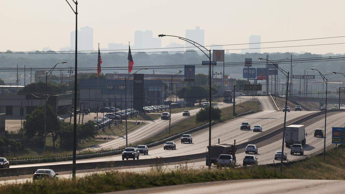 Cars drive on a highway with the downtown skyline in the distance. It's hazy and moody.