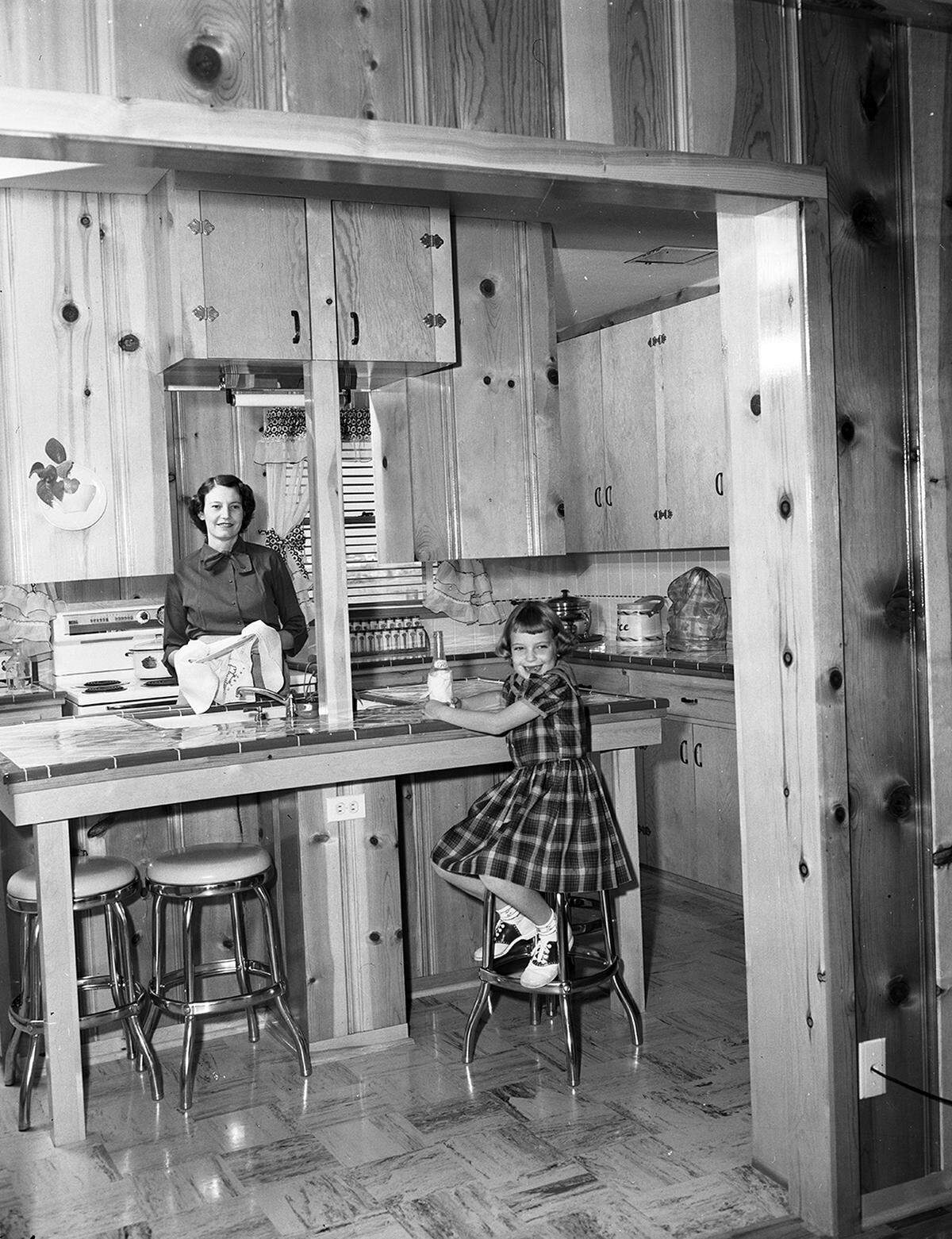 Oct. 29, 1952: Mrs. H. Ward Collier, Jr. and daughter, Connie Anne, look from the kitchen island into the den of their new home in Northglen Addition. The walls and cabinets are distinctly knotted pine.