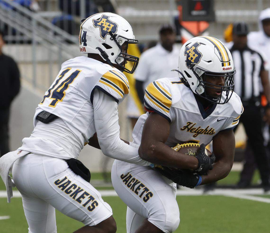 Fort Worth Arlington Heights quarterback Carmelo Carter (14) hands the ball to running back Carson James (1) against Aledo during the first half of a UIL Class 5A Division I Regional on Friday Nov. 28, 2025 at Crowley ISD Multi-Purpose Stadium in Fort Worth, Texas.
