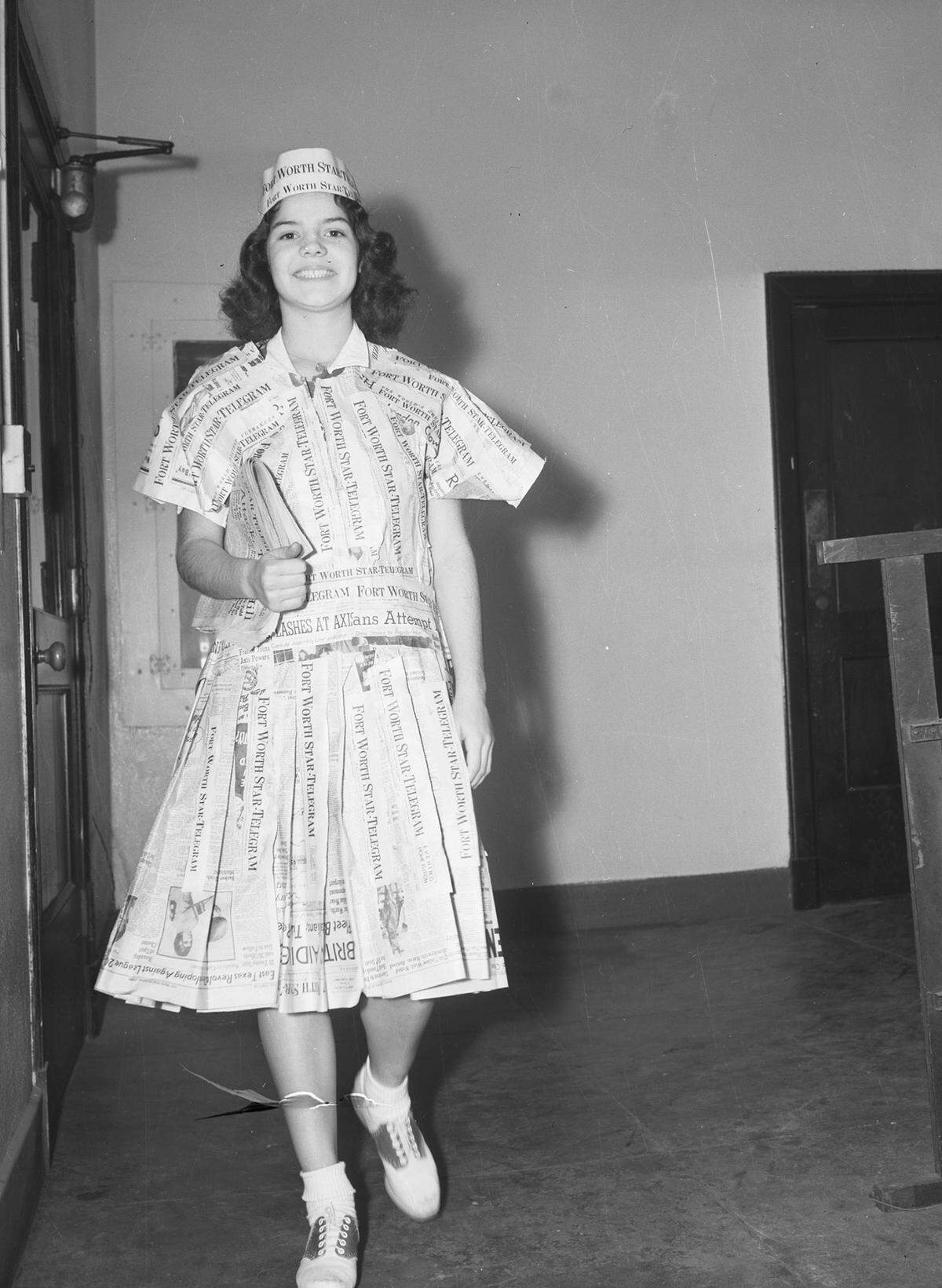 Black and white photograph showing Miss Oyervides as she proudly models her dress and hat made out of newspaper.