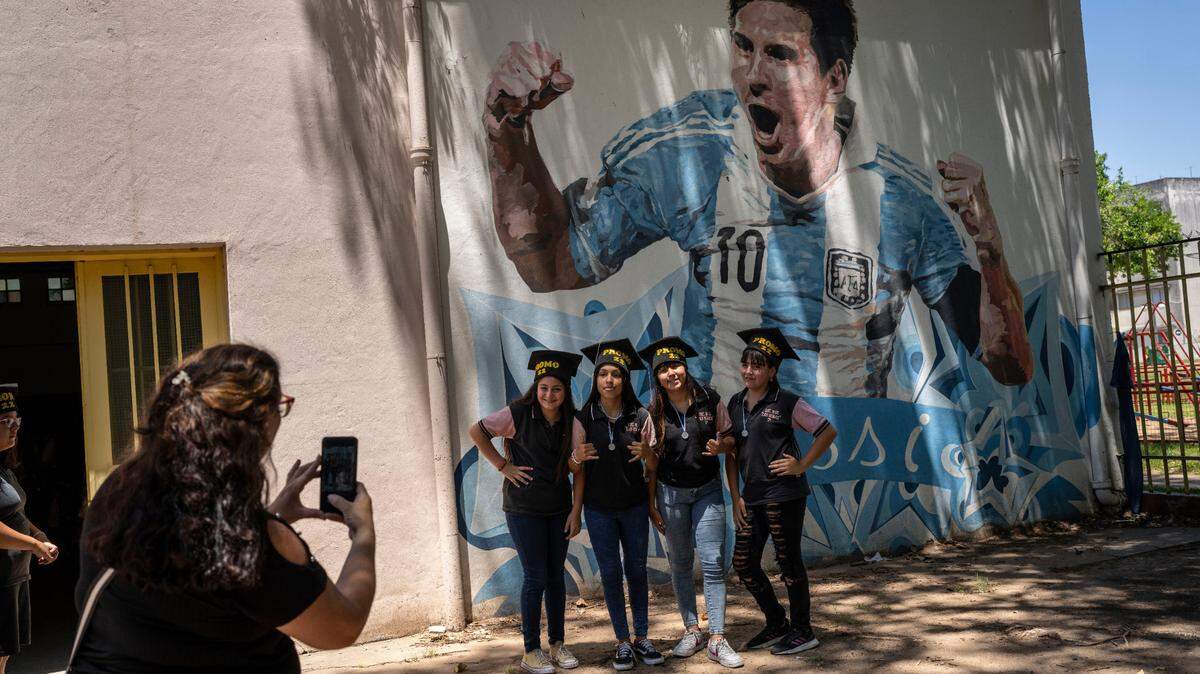 Students graduating from the General Las Heras elementary school, where Lionel Messi also attended school, pose for a group photo wearing their graduation hats by a mural of Messi, on the last day of school in Rosario, Argentina, Wednesday, Dec. 14, 2022.