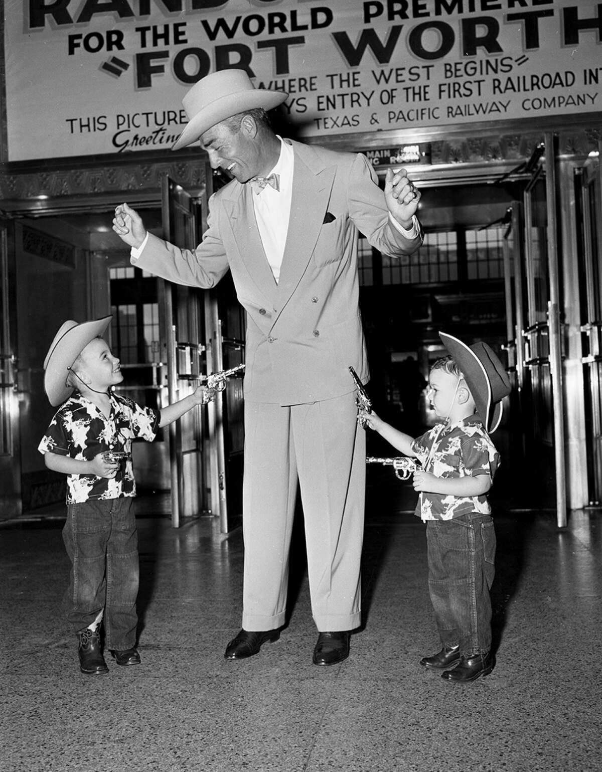 June 11, 1951: Kent, 4, and Kimmie, 2, cowboy sons of Ralph Houps, find it’s not so tough to hold up the screen’s No. 1 Western Star, Randolph Scott. The stickup was staged after Scott’s arrival here for the “Fort Worth” world movie premiere.