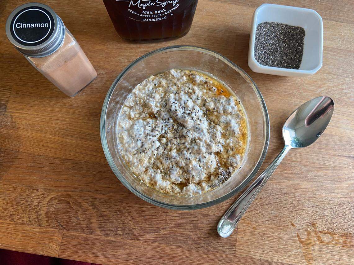 A bowl of overnight oats surrounded by ingredients, such as chia seeds, cinnamon and maple syrup.