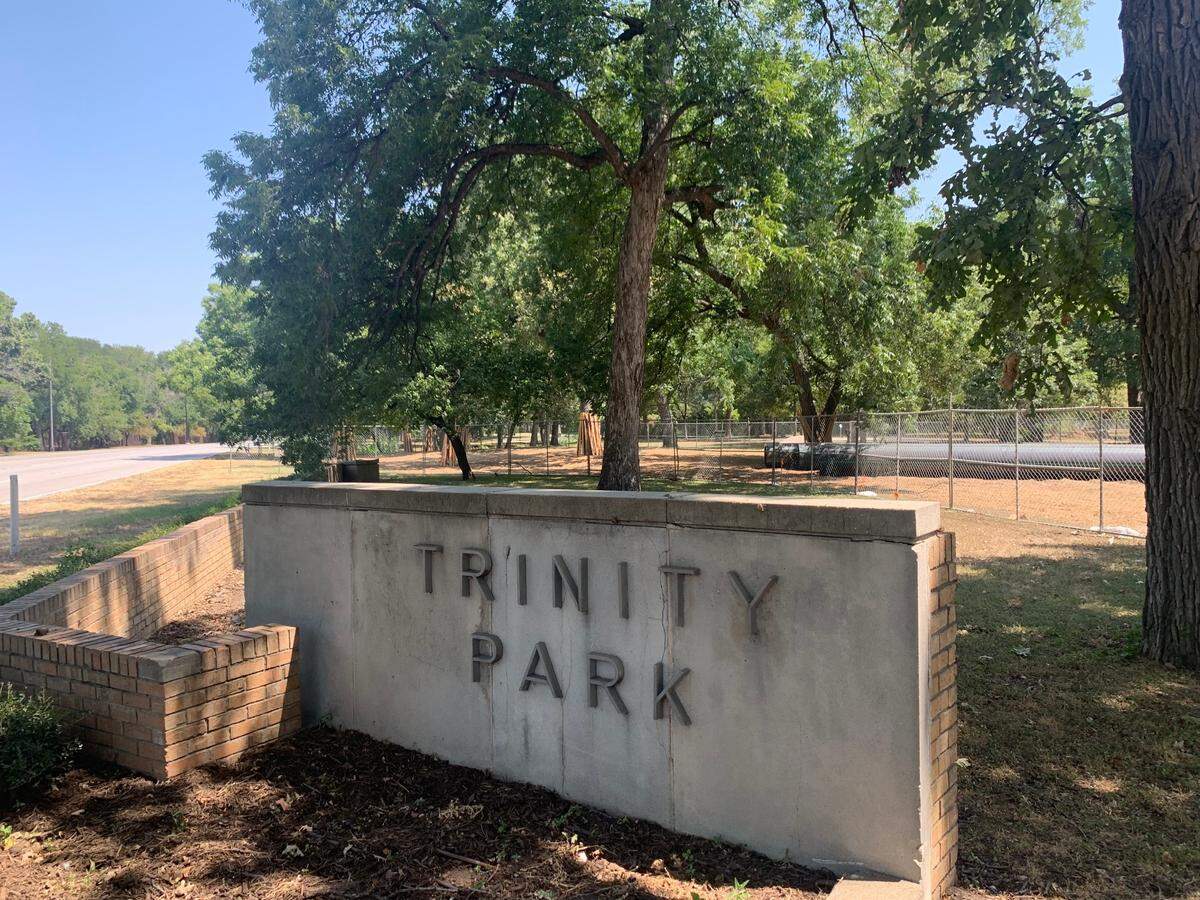 Construction in a section of Trinity Park is fenced off. Trees in the area have wood planks along the trunks.